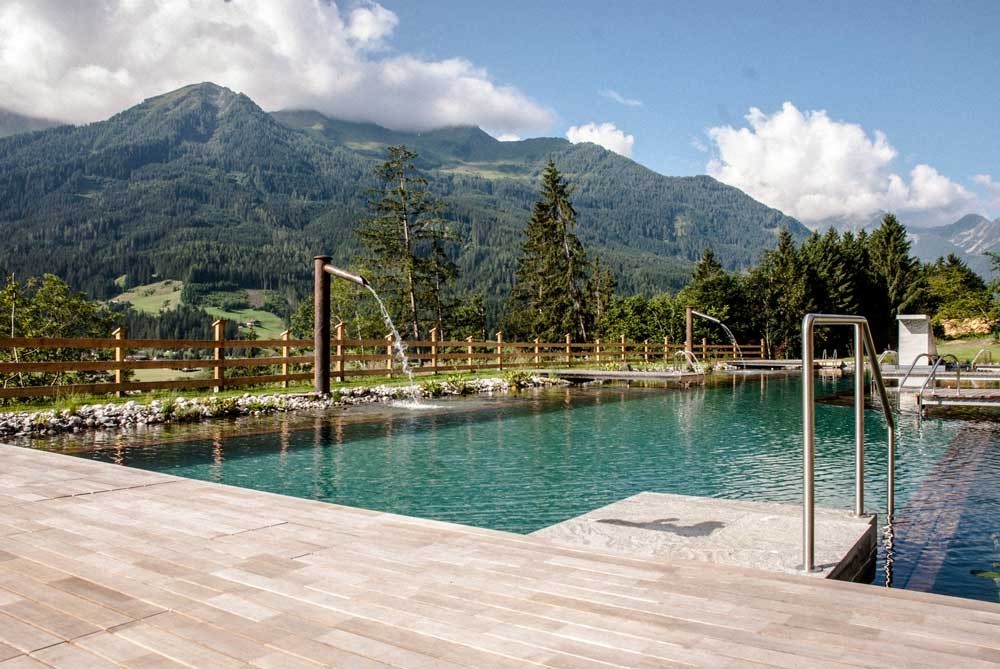 Modern biopool with waterfall and wooden terrace in front of alpine mountain scenery