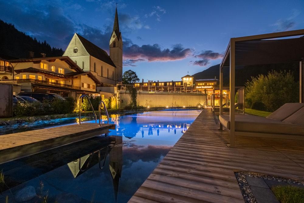 Hotel pool with wood deck at dusk next to a church