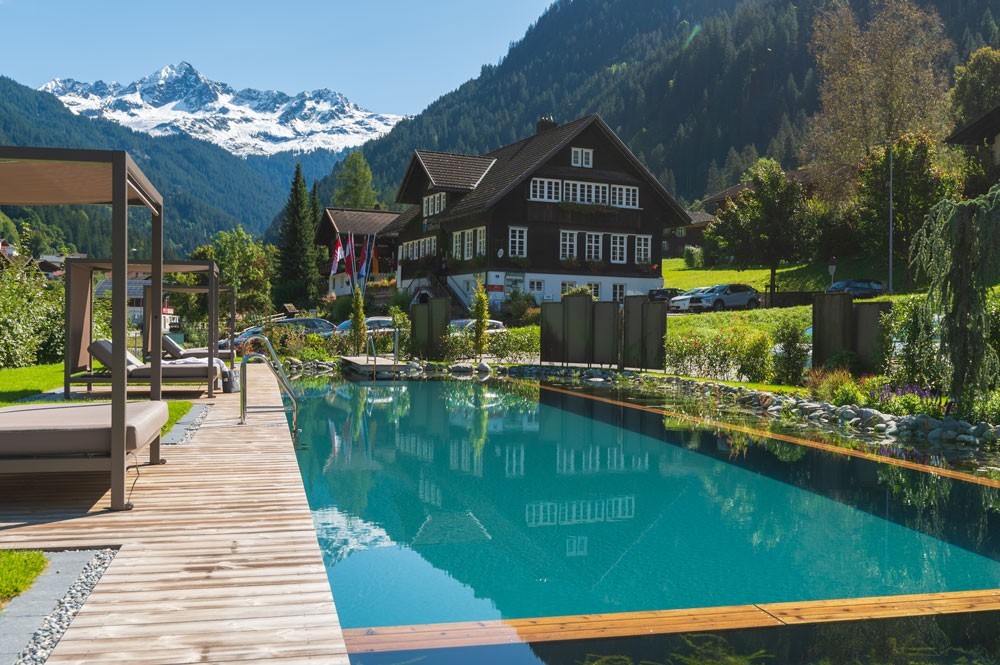 Hotel pool with mountain view in front of an alpine hotel and wood deck