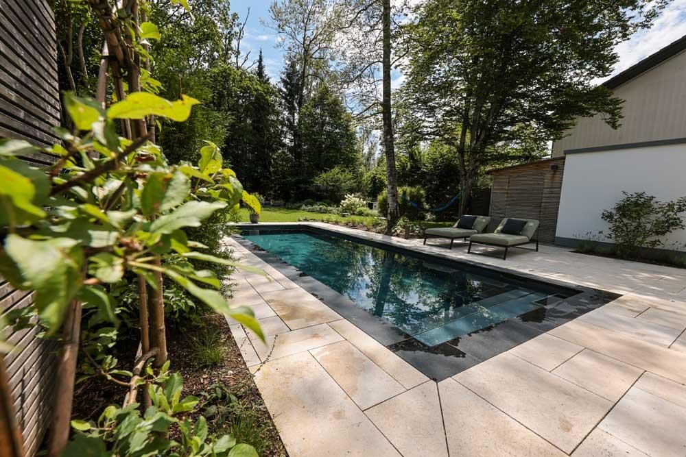 Design pool with loungers and light stone terrace in a green garden