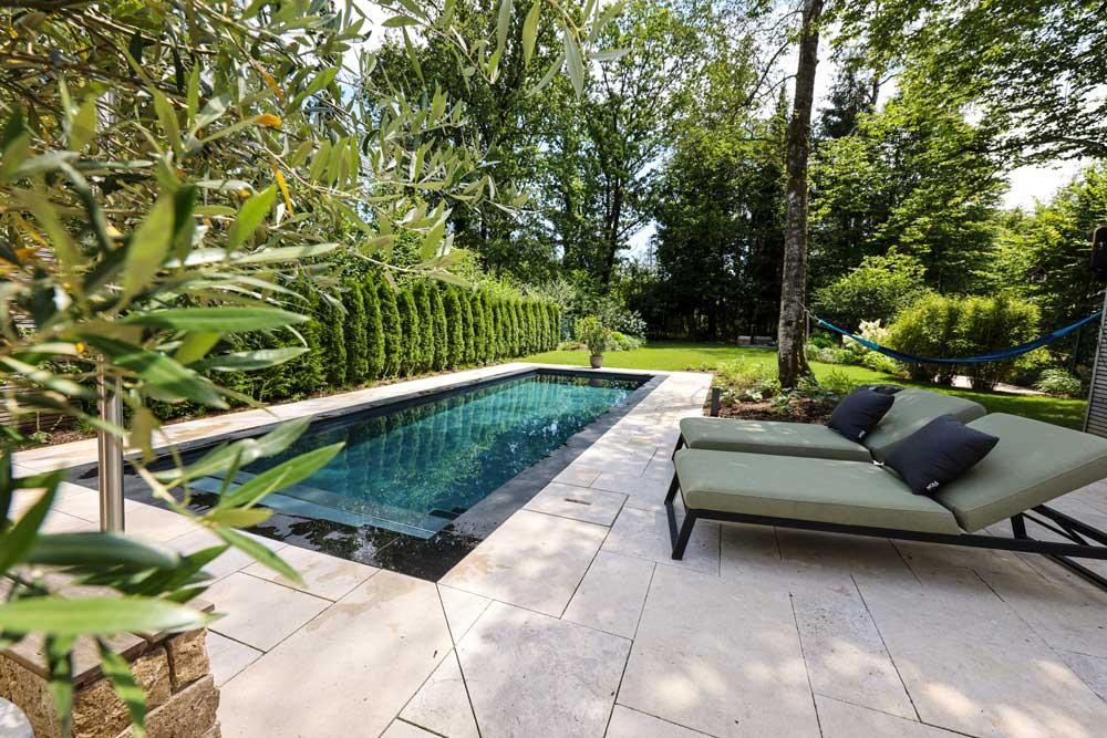 Design pool with light stone terrace and loungers in a quiet garden