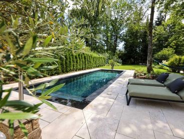Design pool with light stone terrace and loungers in a quiet garden