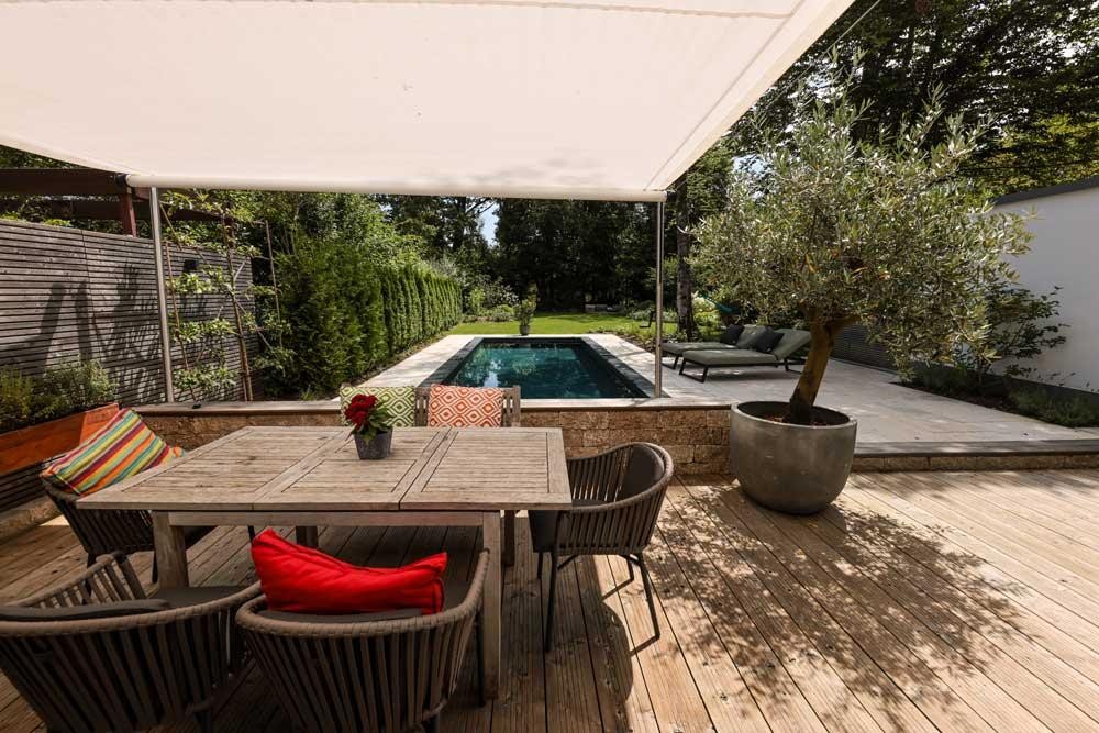 Design pool with wooden terrace, shade sail and dining area in the garden