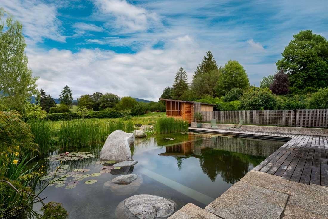 Natural pool with a wooden deck and garden house in an open landscape