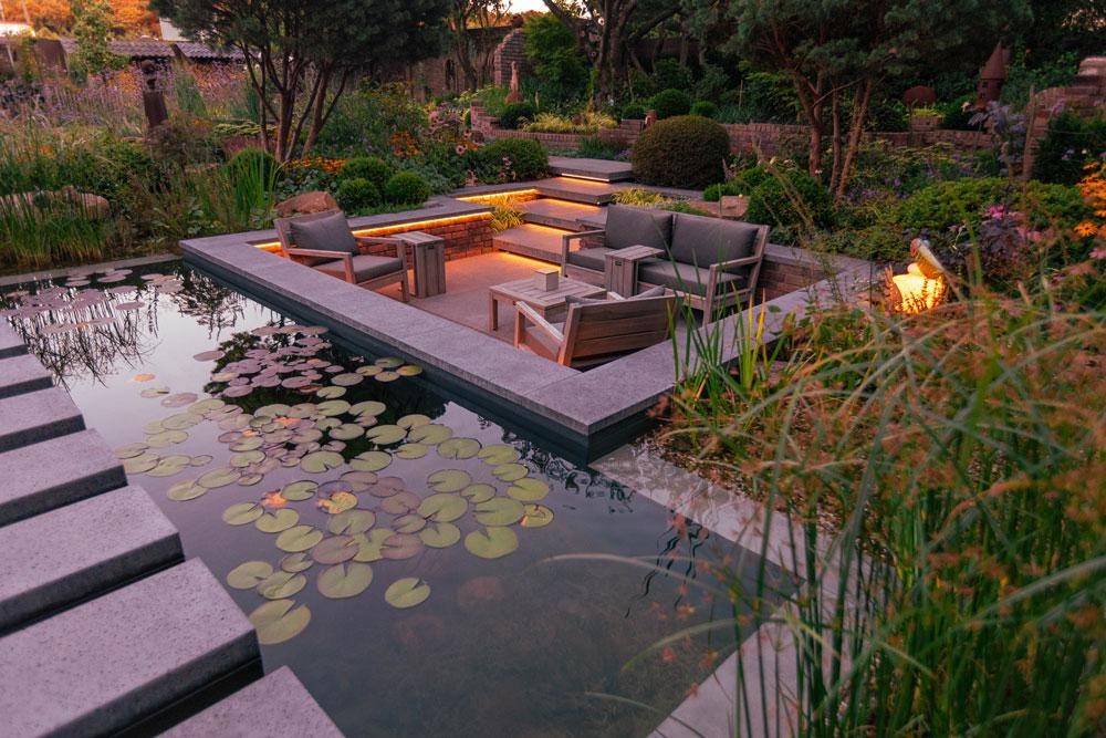 Lounge by natural pool with water lilies and warm evening lighting