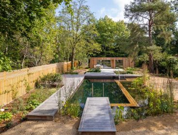 Natural pool with wooden deck in a large urban garden in front of a brick house