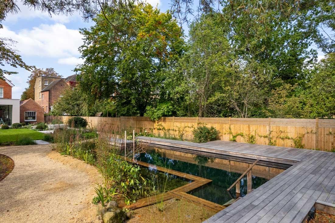 Natural pool with wooden walkway in front of a modern garden house in a green garden