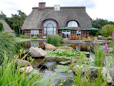 Stunning garden landscape with a traditional thatched house and a natural Swimming Pond