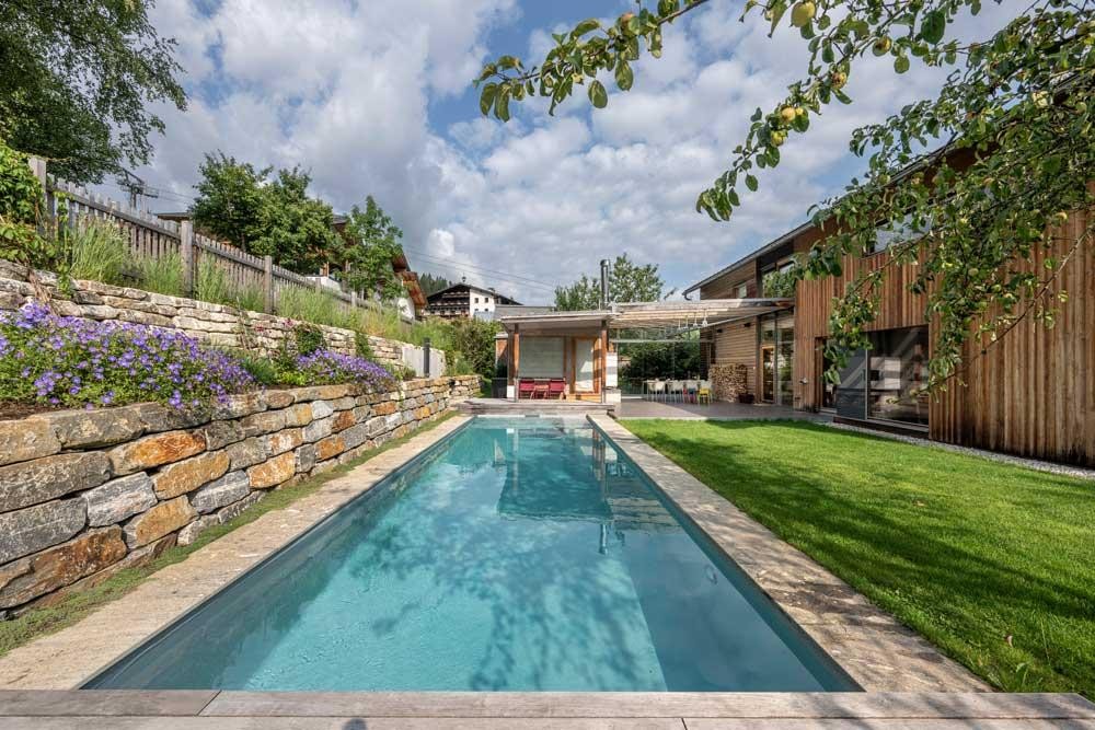 Modern biopool in the garden with wooden house and natural stone wall