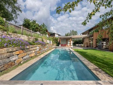 Modern biopool in the garden with wooden house and natural stone wall