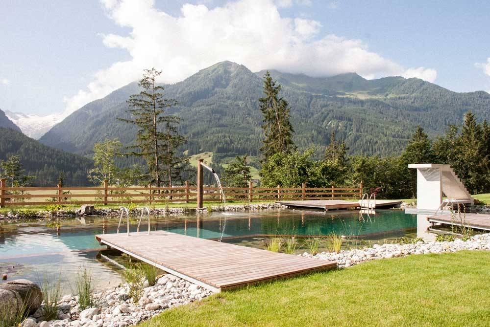 Biopool with wooden deck and waterfall in front of alpine mountain scenery