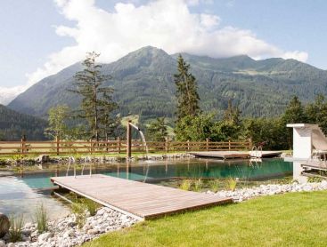 Biopool with wooden deck and waterfall in front of alpine mountain scenery