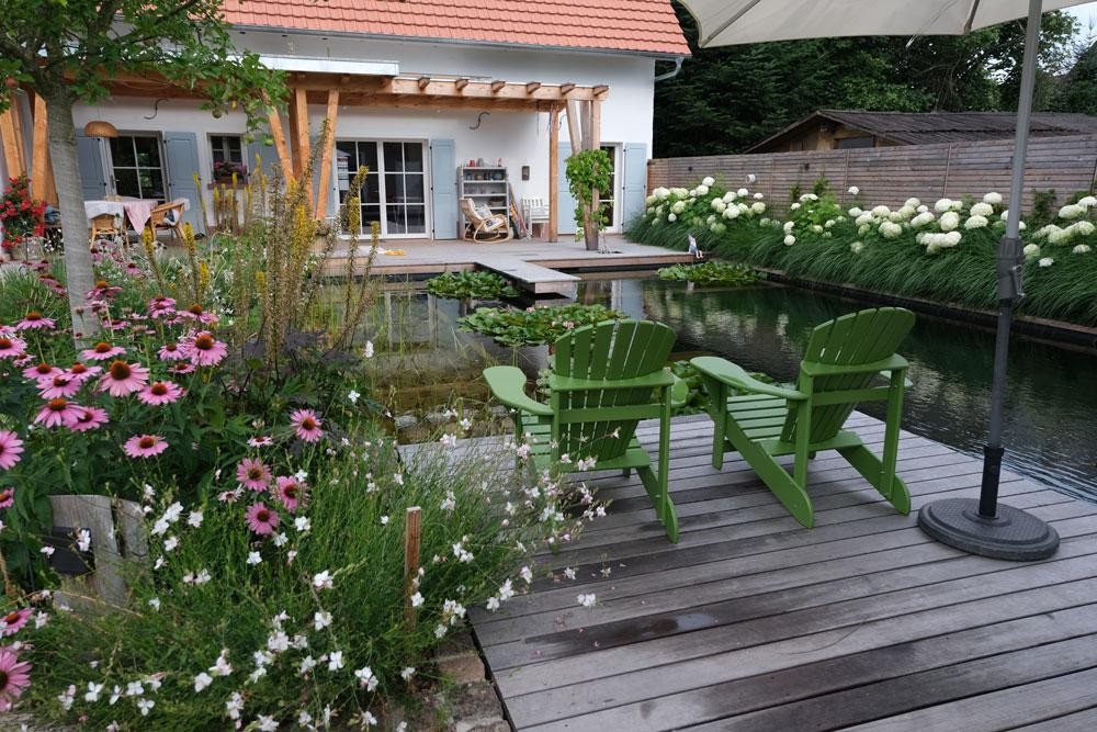 Natural pool with wood deck green chairs and blooming garden