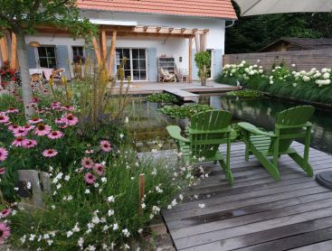 Natural pool with wood deck green chairs and blooming garden