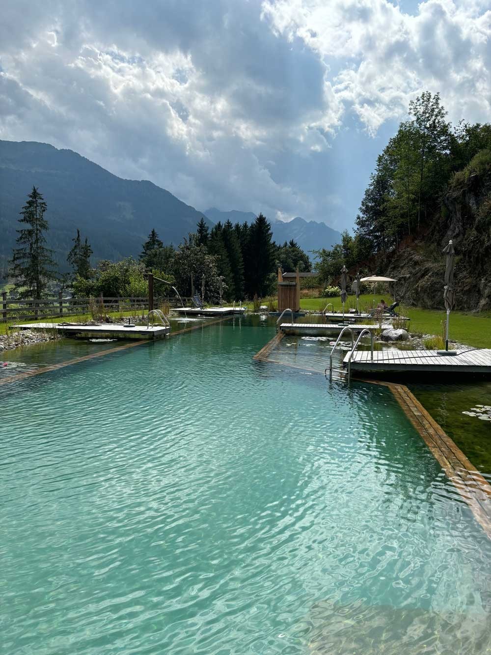Large Swimming Pond with wooden walkways and wellness area in alpine landscape