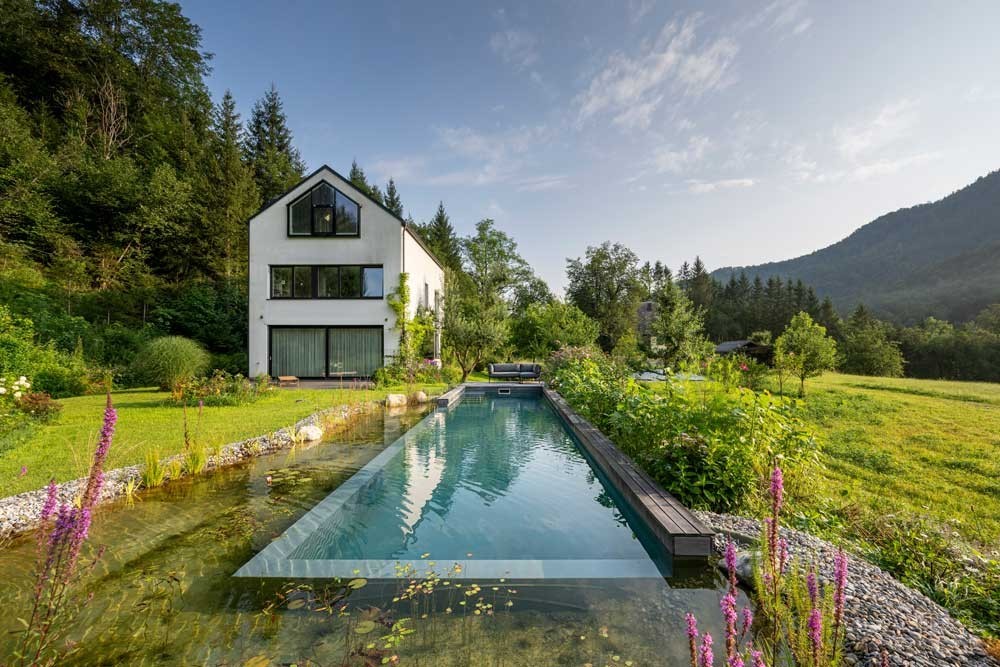 Swimming Pond with wooden deck and regeneration zone in front of a modern house with mountain view