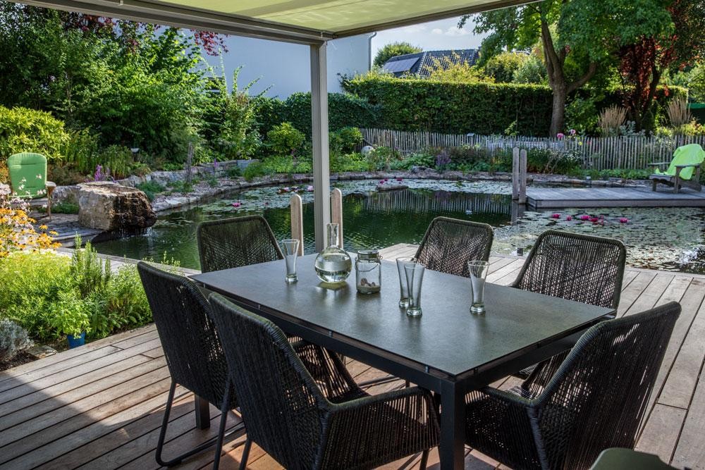 Terrace with dining table and view of swimming pond in natural garden